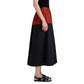 A person stands in profile wearing a sleeveless black top, the Nyla Skirt by Proenza Schouler White Label in color-blocked black and rust poplin, and black sandals against a white background.