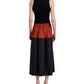 Facing away, the person wears a sleeveless black top with Proenza Schouler White Label's Nyla Skirt—a long, color-blocked design featuring a rust band at the waist—paired with black sandals.