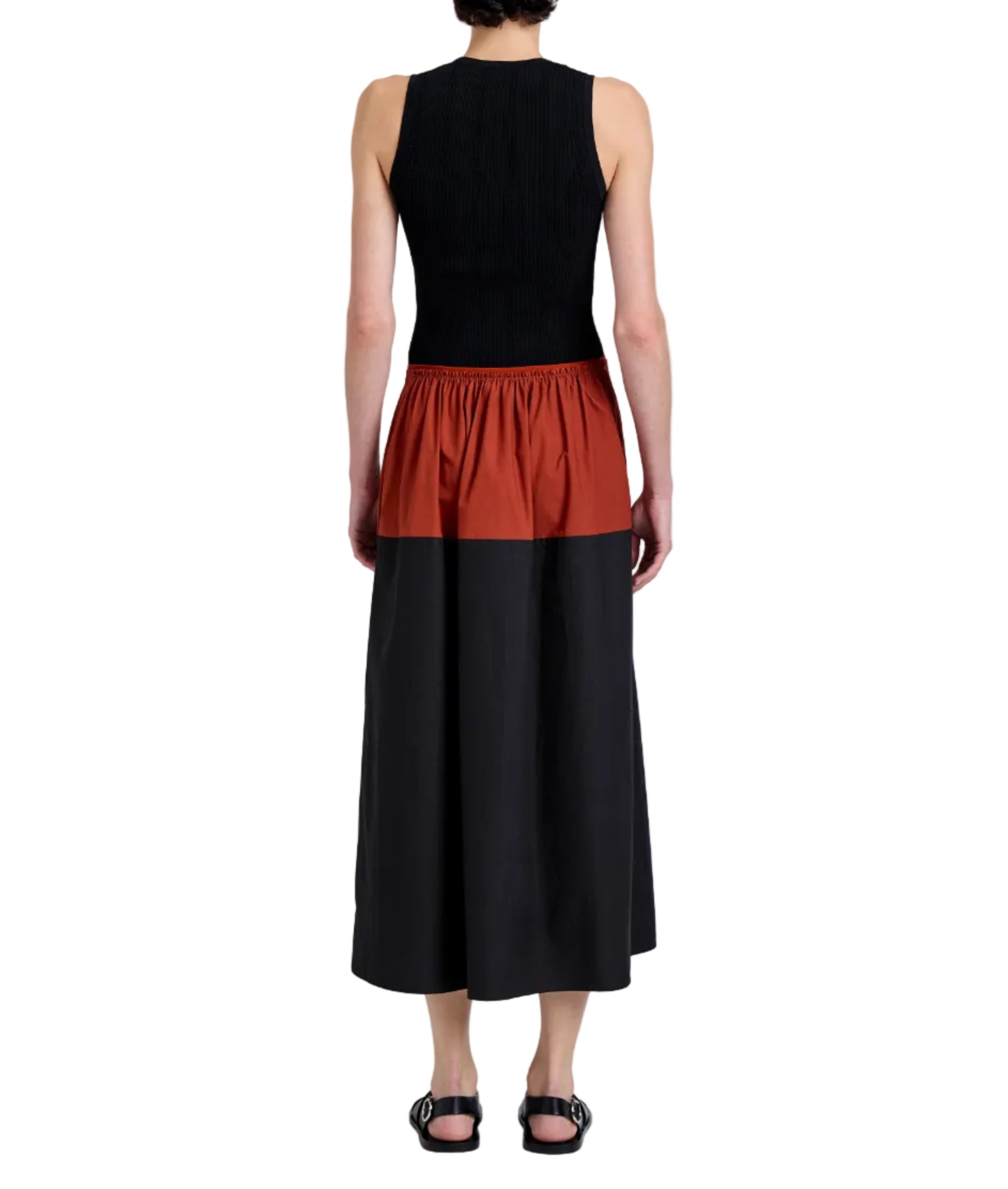Facing away, the person wears a sleeveless black top with Proenza Schouler White Label's Nyla Skirt—a long, color-blocked design featuring a rust band at the waist—paired with black sandals.