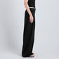A person stands in profile against a plain light background, wearing the Coralie Pant by Proenza Schouler White Label and a black sleeveless top.