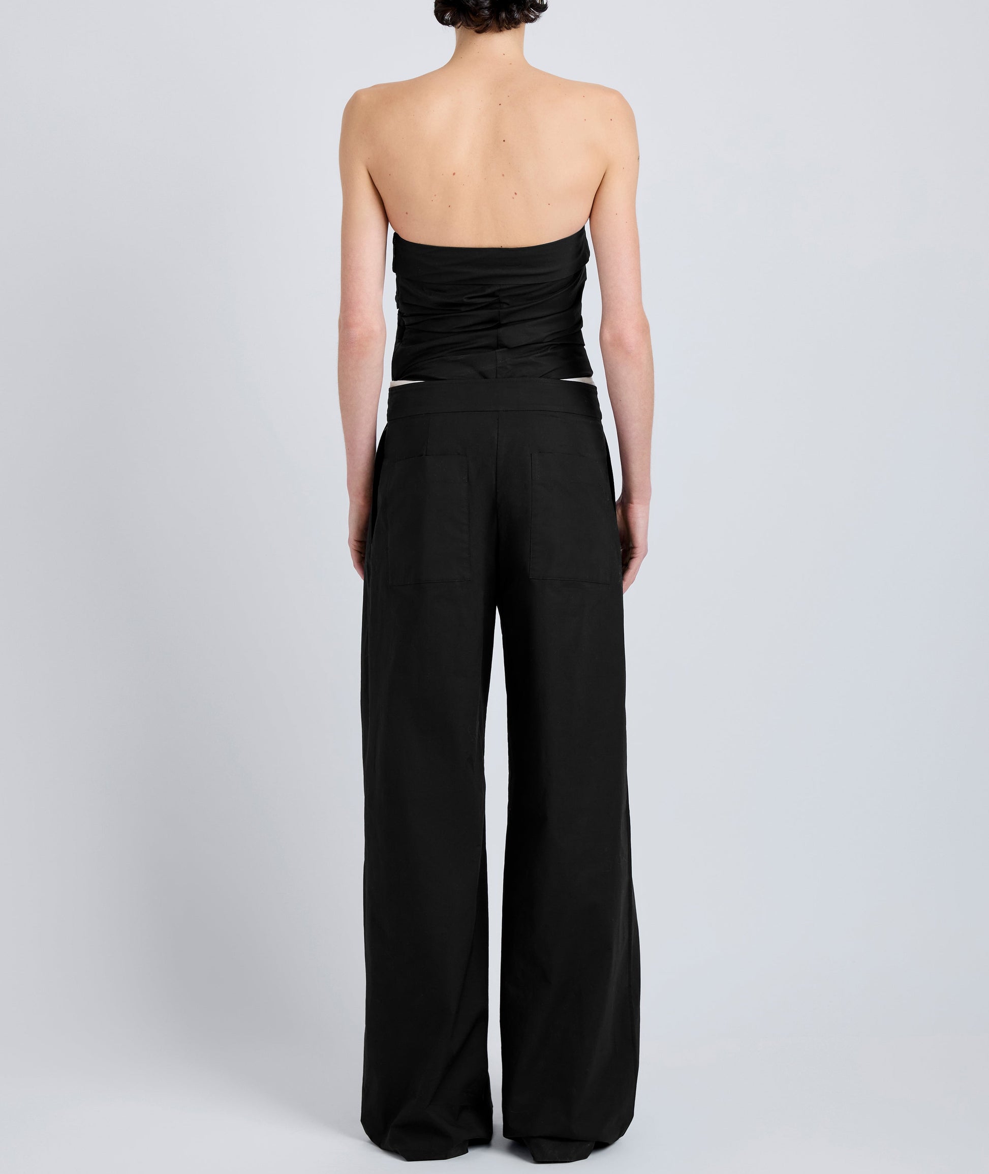 A person stands with their back to the camera, wearing a black strapless top and Proenza Schouler White Label Coralie Pant—high-waisted with a wide-leg silhouette—against a plain light background.