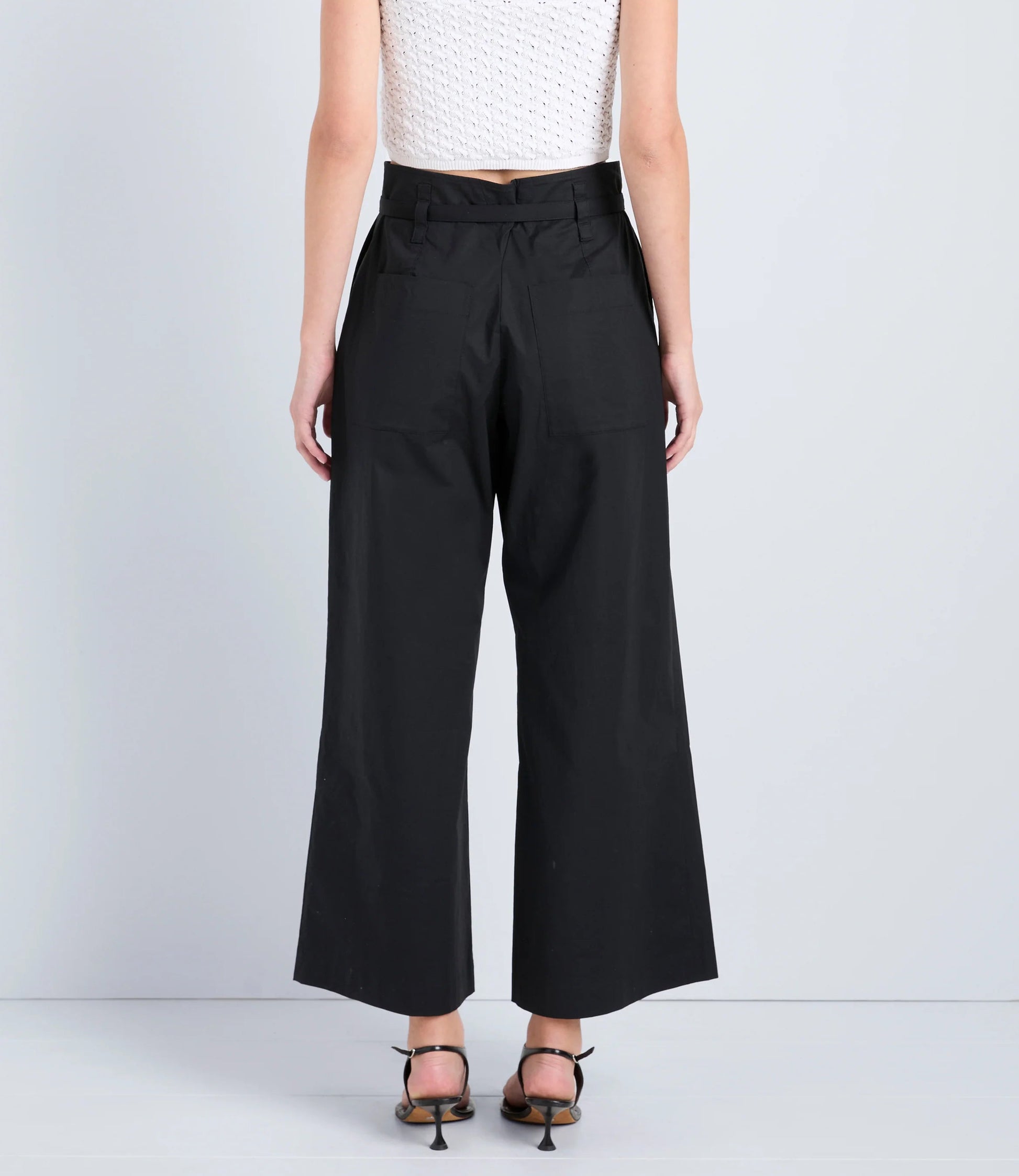 A person stands with their back to the camera against a plain background, wearing Proenza Schouler White Label Cropped Raver Pant in black and heeled sandals.