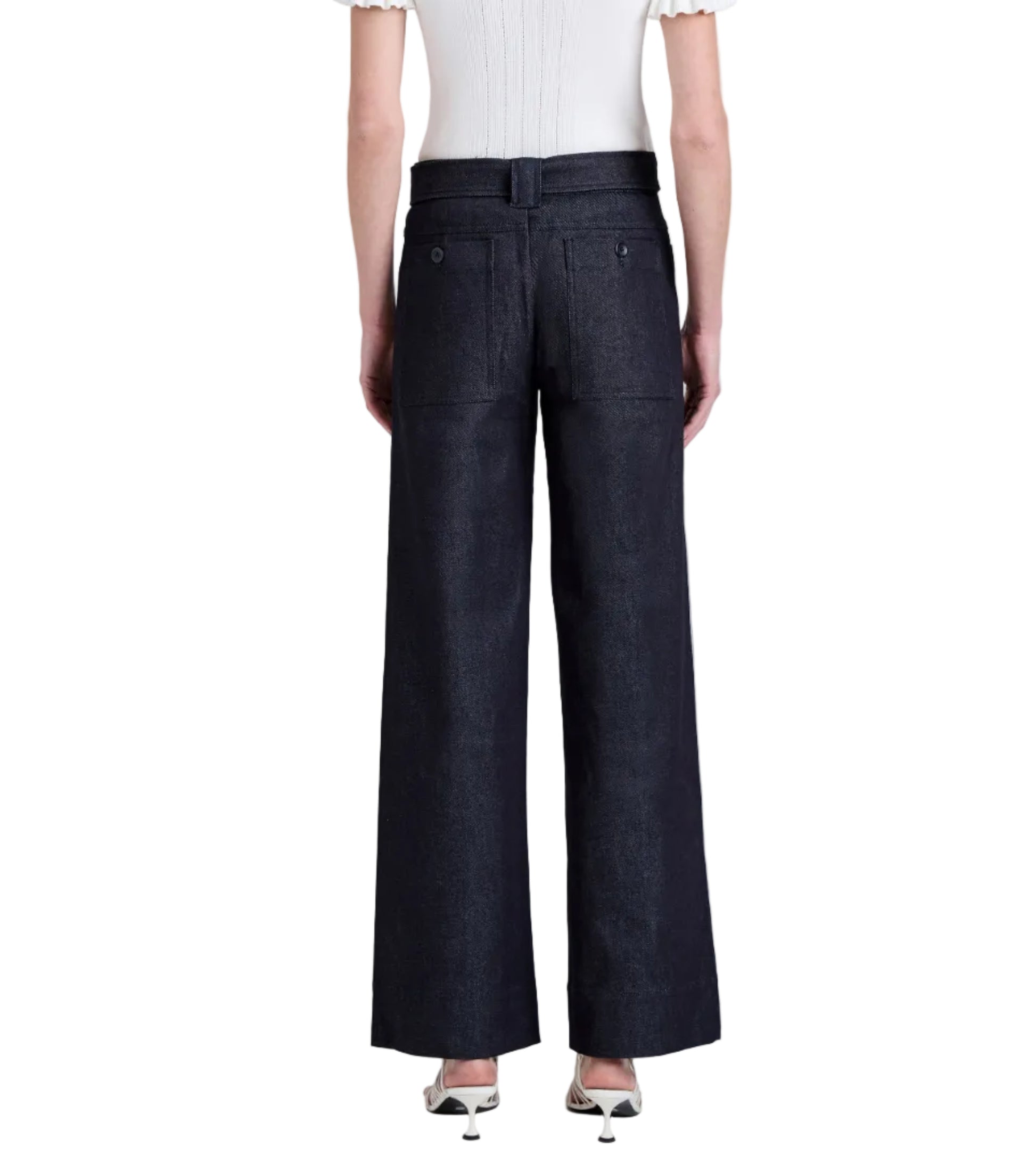 A person, seen from the back, wears a short-sleeve white top and Proenza Schouler White Label Lina Pant—high-waisted, wide-leg dark denim jeans—paired with white heeled shoes.
