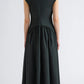 A woman stands facing away, wearing the Proenza Schouler White Label Nyssa Stretch Cotton Dress—a dark green, short-sleeved, midi-length dress for women featuring a fitted bodice and gathered skirt crafted from soft stretch cotton—stylishly paired with brown block-heeled shoes.