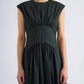 Wearing the Proenza Schouler White Label Nyssa Stretch Cotton Dress, a sleeveless dark green women's dress featuring gathered fabric details at the shoulders, waist, and skirt, the person stands against a plain light background.