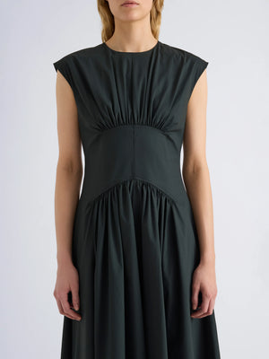 Wearing the Proenza Schouler White Label Nyssa Stretch Cotton Dress, a sleeveless dark green women's dress featuring gathered fabric details at the shoulders, waist, and skirt, the person stands against a plain light background.