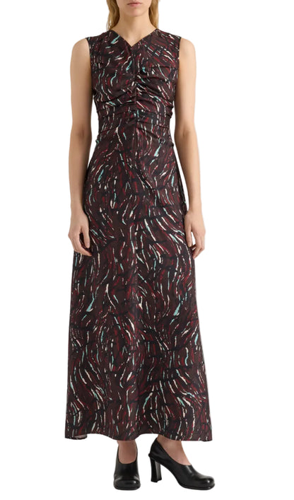 A woman wearing the Clem Dress by Proenza Schouler White Label—a sleeveless, fitted, ankle-length dress crafted from printed soft twill with a swirling red, white, and teal pattern—pairs it with black heeled shoes while standing against a white background.