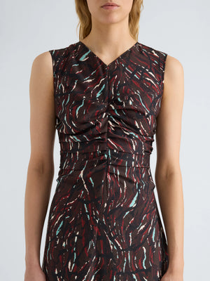 A woman wears the Clem Dress by Proenza Schouler White Label, a sleeveless, printed soft twill dress designed with gathered fabric at the chest and waist. The dress showcases red, white, and teal abstract streaks against a dark background.