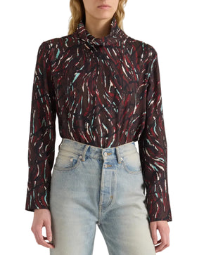 A person is wearing the Ansel Printed Soft Twill Top by Proenza Schouler White Label—a high-neck, long-sleeve blouse featuring red, white, and teal streaks—paired with light blue high-waisted jeans.