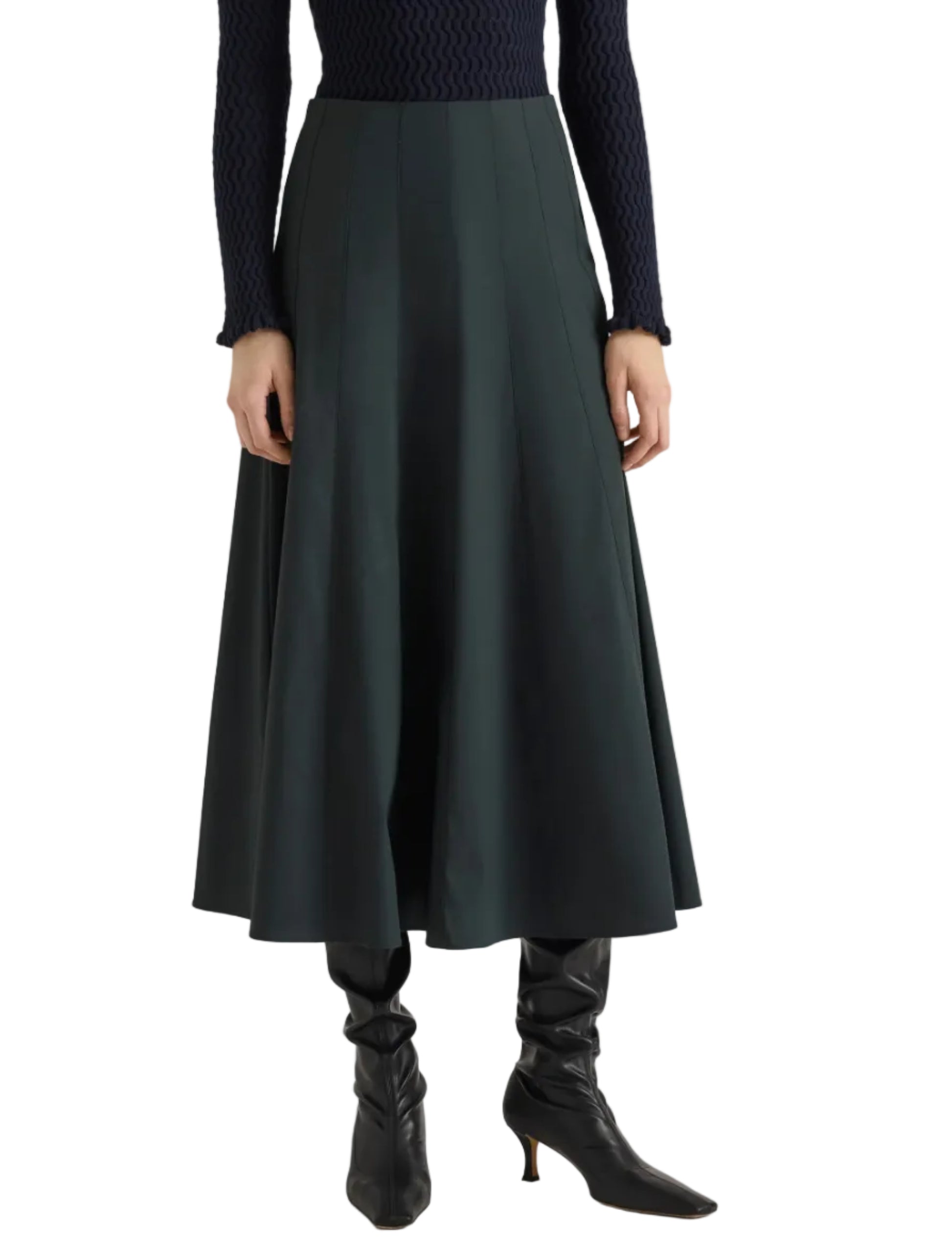 A person stands against a white background wearing the Proenza Schouler White Label Heidi Stretch Cotton Skirt in dark green, styled with a navy textured sweater and black heeled boots.