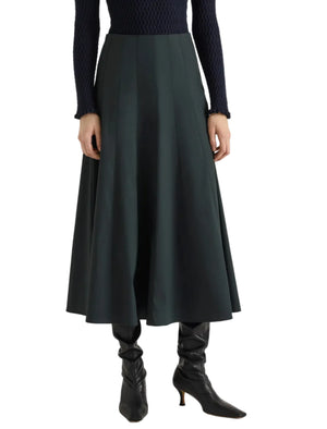 A person stands against a white background wearing the Proenza Schouler White Label Heidi Stretch Cotton Skirt in dark green, styled with a navy textured sweater and black heeled boots.