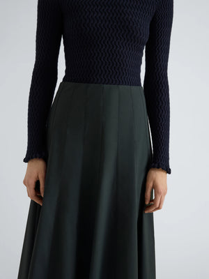 A person wears a textured long-sleeve black top paired with the Proenza Schouler White Label Heidi Stretch Cotton Skirt, a high-waisted, dark skirt; only their torso and upper legs are visible against a plain background.