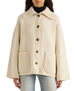 A person wearing a cream-colored Proenza Schouler White Label Nelly Melange Merino Jacket, featuring a button-front closure, large front pockets, and wide sleeves, paired with light blue jeans.