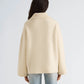 Facing away, the person is wearing the cream-colored, oversized Nelly Melange Merino Jacket by Proenza Schouler White Label, featuring a ribbed collar and paired with light blue jeans against a plain background.