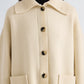 A person wearing the Nelly Melange Merino Jacket by Proenza Schouler White Label, a cream-colored button-up knit cardigan featuring large front pockets and a wide collar, styled over a black turtleneck.