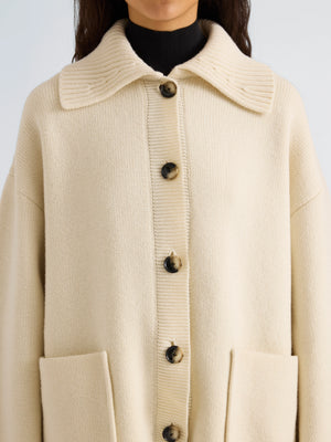 A person wearing the Nelly Melange Merino Jacket by Proenza Schouler White Label, a cream-colored button-up knit cardigan featuring large front pockets and a wide collar, styled over a black turtleneck.