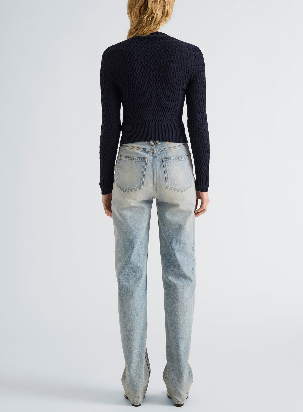 Back view of a person wearing a dark navy textured Proenza Schouler White Label Marci Cardigan with a crew neckline and long sleeves, paired with light-wash blue jeans.