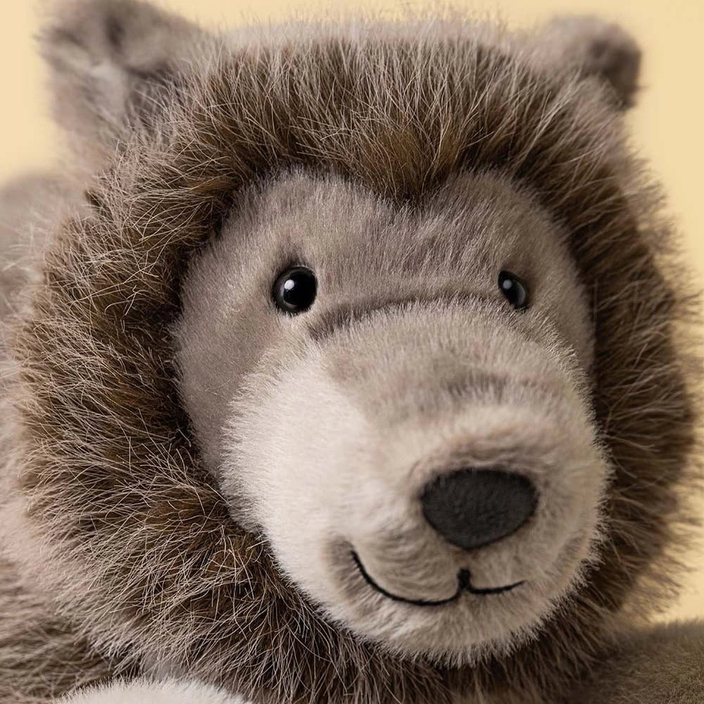Close-up of Jellycat’s Ulrich Wolf, a gray stuffed animal with black eyes, fluffy fur, and a stitched smile against a plain background.