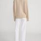 A person faces away, wearing The Stroll white mid-rise jean pants by Frame and a beige sweater, crafted from premium cotton against a plain light background.