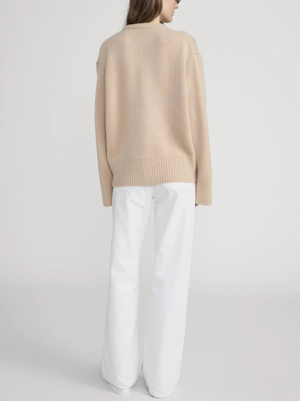 A person faces away, wearing The Stroll white mid-rise jean pants by Frame and a beige sweater, crafted from premium cotton against a plain light background.