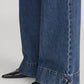 Close-up of a person wearing Frame's The Slice Flare luxury wide-leg blue jeans featuring small hem slits, paired with black pointed-toe shoes.