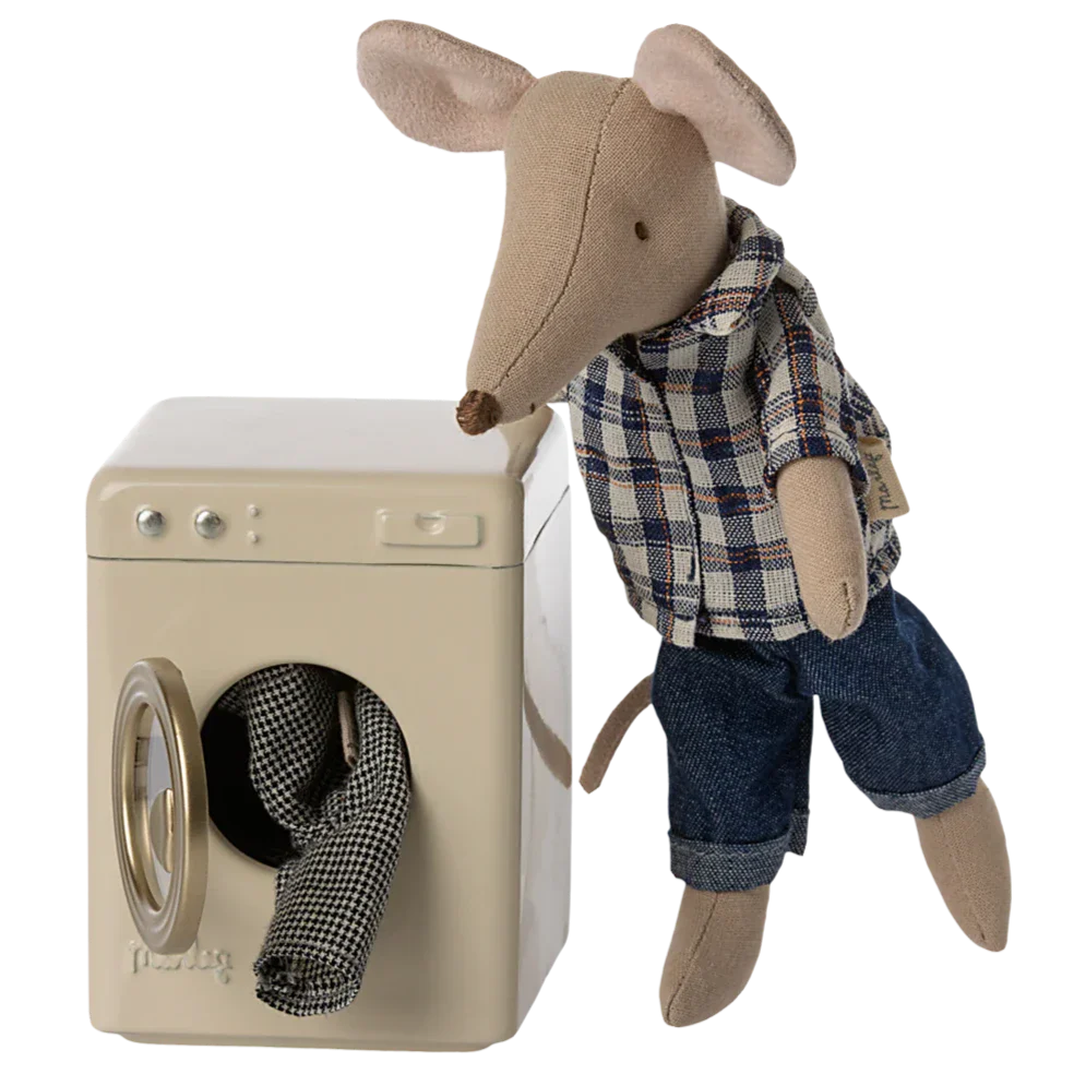 A Maileg mouse in a plaid shirt and jeans stands beside the Maileg Washing Machine, Mouse, with clothes partly inside, part of the adorable mouse family tending to their toy appliances.