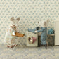 Two fabric mice in a dollhouse setting: one mouse in pajamas stands by a Maileg Washing Machine, Mouse by Maileg, while another mouse in a dress holds an ironing board. The charming scene depicts the mouse family diligently doing laundry.