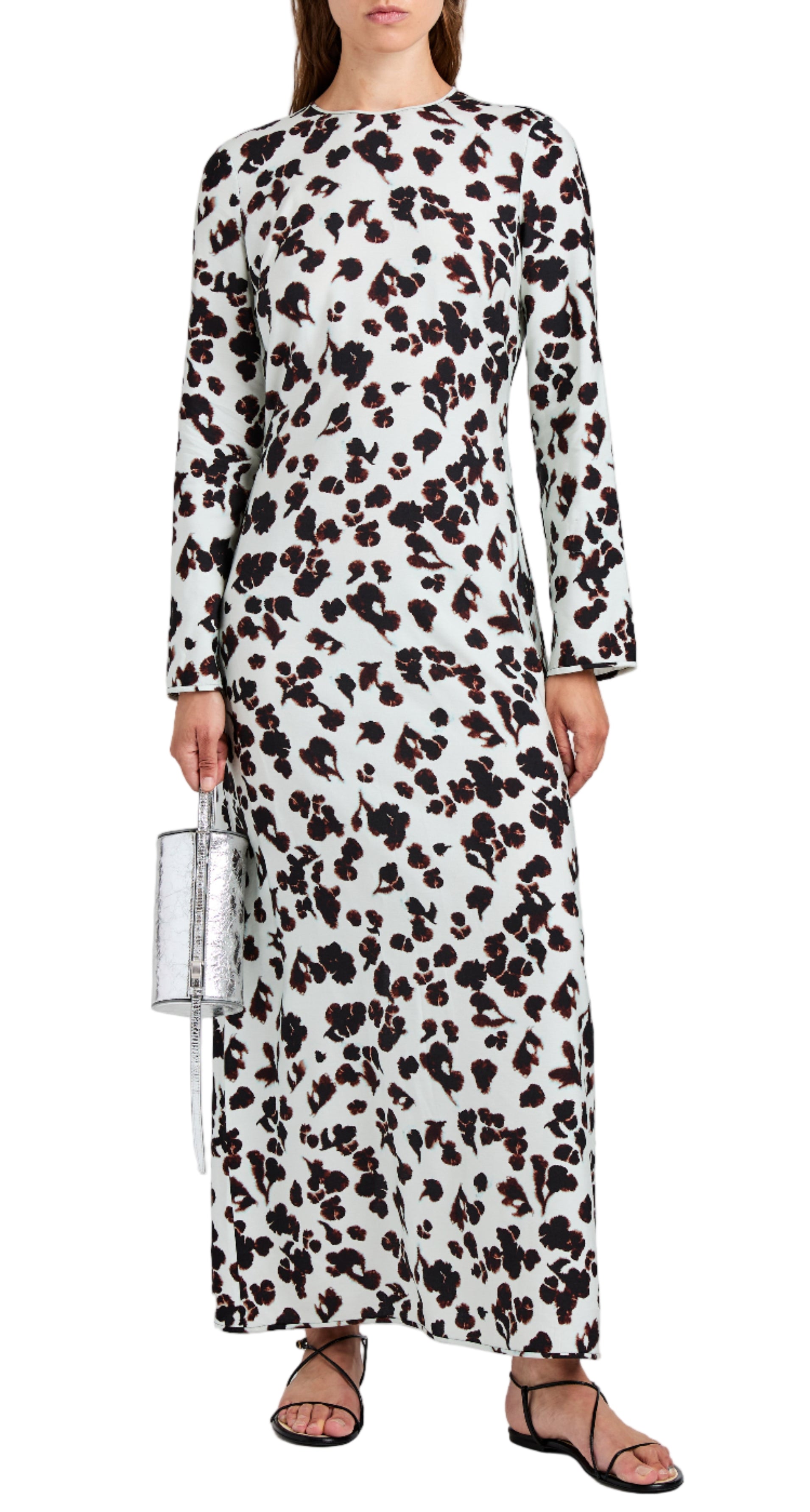 A woman wears the Proenza Schouler White Label Waverly Dress—an ankle-length, long-sleeve white dress with black and brown abstract print—styled with black sandals and a silver handbag.