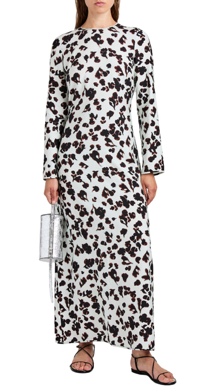 A woman wears the Proenza Schouler White Label Waverly Dress—an ankle-length, long-sleeve white dress with black and brown abstract print—styled with black sandals and a silver handbag.