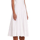 A woman in a white Staud Wells Dress paired with brown knee-high heeled boots, standing against a plain background.