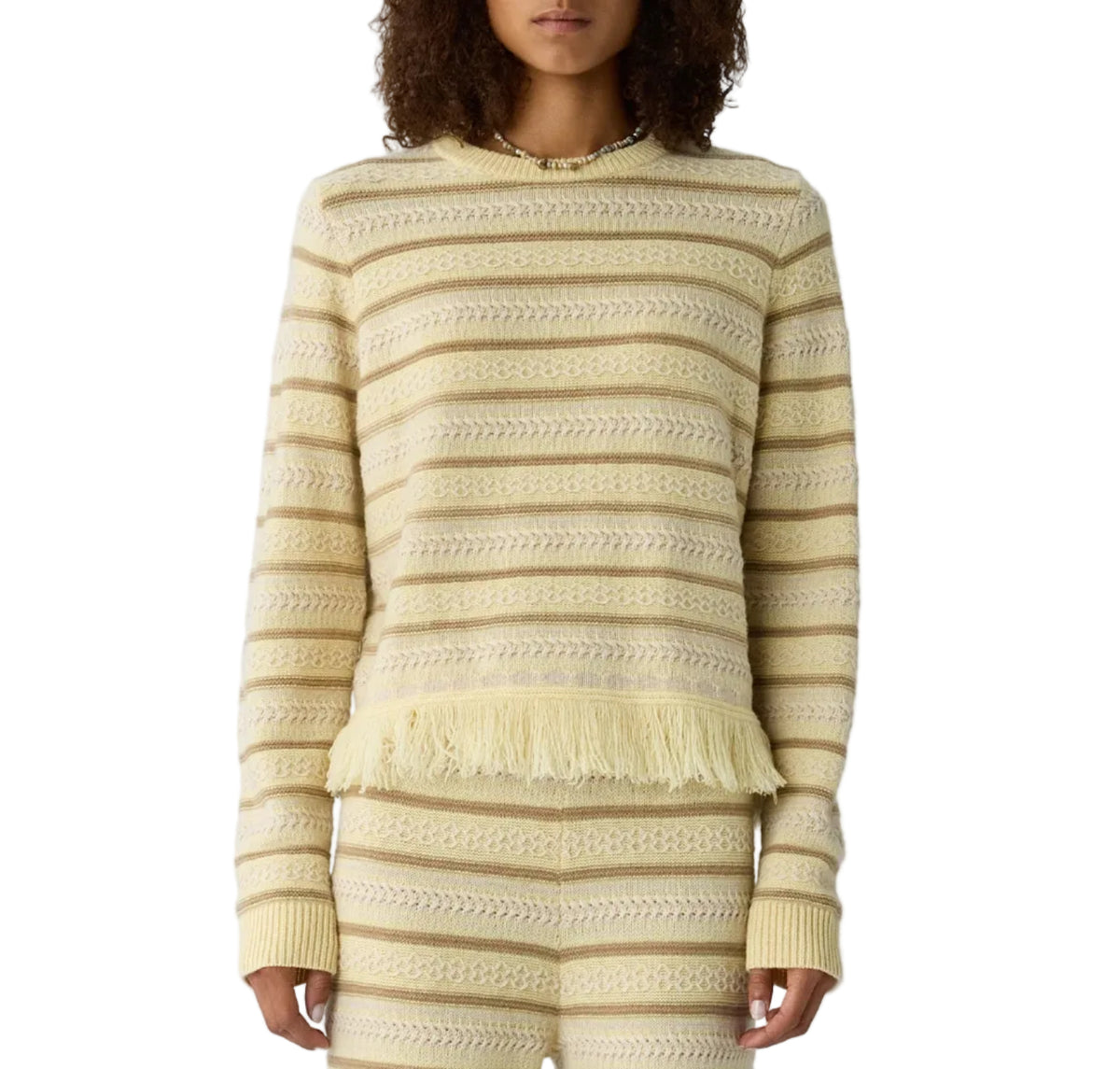 Someone wears the Western Stripe Crew by Guest in Residence—a cream and beige striped sweater with a fringed hem—paired with matching knit pants.