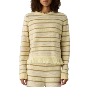 Someone wears the Western Stripe Crew by Guest in Residence—a cream and beige striped sweater with a fringed hem—paired with matching knit pants.