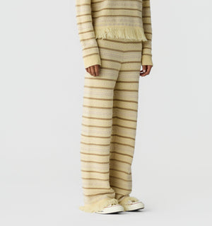 Model wearing the Western Stripe Pant by Guest in Residence, paired with a matching beige and cream striped knit sweater, against a plain white background.