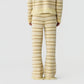 A person stands facing away in a cream and beige knit sweater and the Western Stripe Pant by Guest in Residence, featuring fringe details, against a white background.