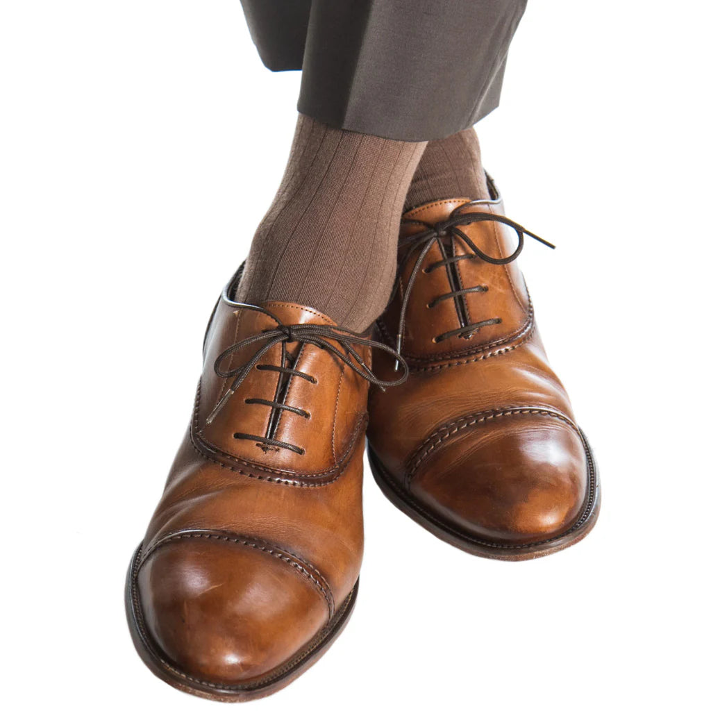 A person wearing brown dress shoes, dark trousers, and Dapper Classics Mushroom Solid Ribbed Fine Merino Wool Sock (Linked Toe Mid-Calf), standing on a white background.