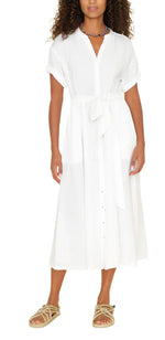 A person wearing the Xirena Cate Dress, a white, short-sleeve, knee-length garment made of washed cotton gauze with side seam pockets, paired with beige sandals from Xirena.