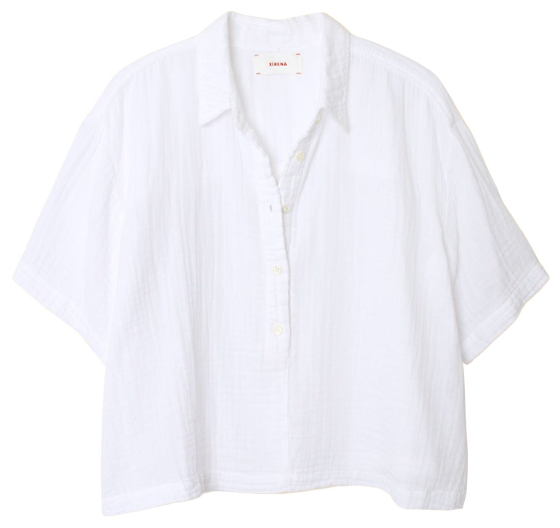 The Xirena Ansel Top by Xirena is a white, short-sleeved, button-up shirt with a collar and a relaxed fit. Crafted from lightweight cotton poplin, made in Los Angeles, it features a lightly textured fabric and includes a tag inside the collar.