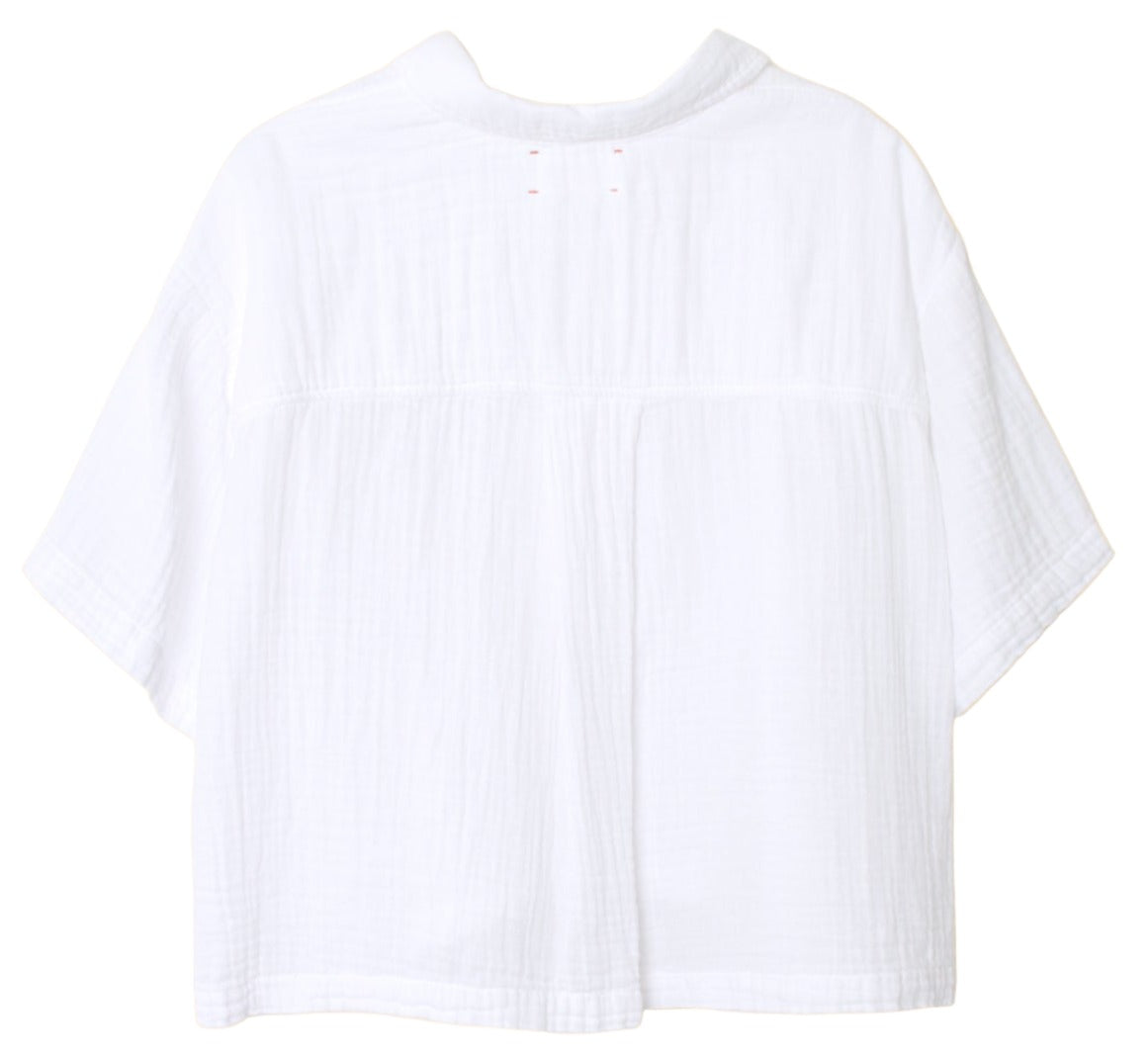 The Xirena Ansel Top, a white short-sleeve shirt with a collar, is shown from the back. This short boxy top by Xirena is meticulously crafted in Los Angeles from lightweight cotton poplin, offering a textured fabric that exudes both comfort and style.