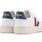 A pair of Veja Men's V-12 Leather Sneakers with navy blue heel tabs and red "V" logos on the sides, crafted from leather and organic cotton, viewed from the back. The sneakers are displayed against a plain white background.