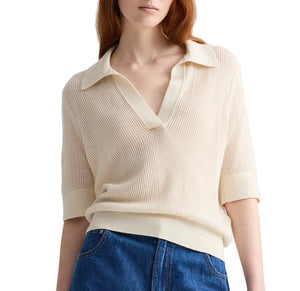 A person wearing TWP’s The Polo, a cream-colored Italian cashmere top with a relaxed fit, short sleeves, and a collared deep V-neck, paired with blue jeans.