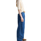 A person stands sideways against a white background, wearing TWP's The Polo knit top in cream with short sleeves and a relaxed fit, paired with wide-leg blue jeans and brown shoes.