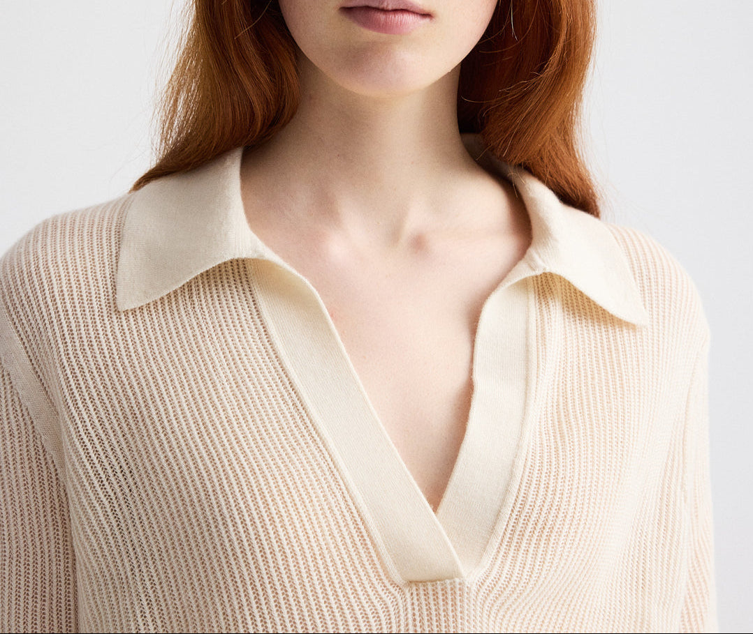 A person with long reddish hair wears The Polo by TWP—a cream-colored, ribbed knit short-sleeve sweater featuring a deep V-neck and wide collar.