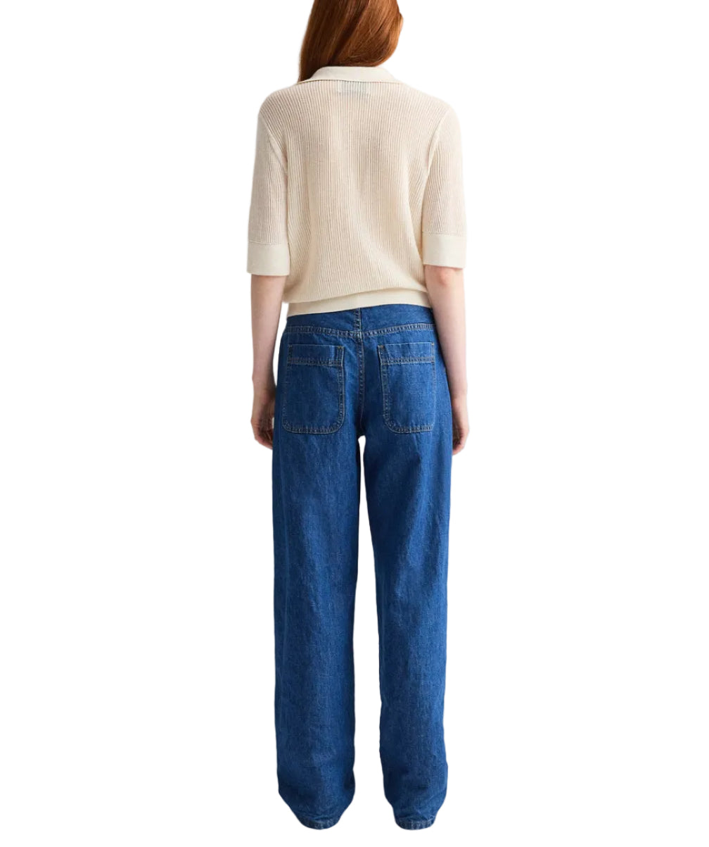 A person stands facing away, wearing TWP's The Polo—a short-sleeve Italian cashmere sweater with a relaxed fit—paired with loose blue jeans, set against a white backdrop.