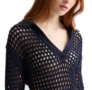 A woman with long red hair wears the Unspoken Truth Polo by TWP, a navy blue open-knit sweater with a deep V-neck, collar, and relaxed fit.