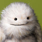 The Jellycat Bretti Yeti, a fluffy white and grey plush toy with black button eyes and a stitched smile, stands as a guardian against a plain green background.