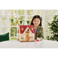 A young girl smiles while sitting at a table with a Calico Critters Red Roof Cozy Cottage and a small Calico Critters Chocolate Rabbit girl figurine in front of her.