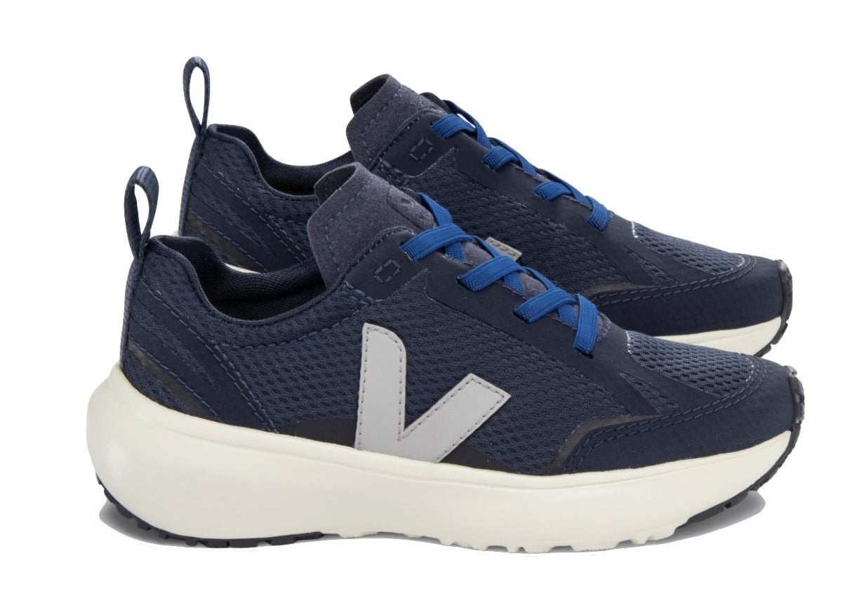 The Veja Junior Canary Alveomesh Sneaker from Veja is a pair of navy blue sneakers featuring white soles, blue laces, a white "V" logo on the side, and a pull tab at the back. These eco-friendly shoes are made from Amazonian rubber and recycled polyester.