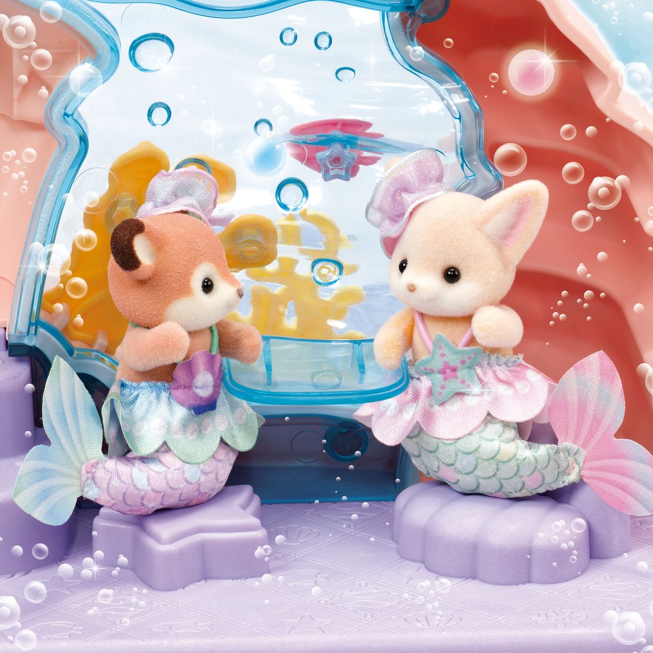 Two Calico Critters Baby Mermaid figures sit on purple seats in the Baby Mermaid Castle playset, featuring an underwater theme with bubbles and pastel decorations.