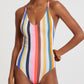 A woman wears the Lemlem Retiro One Piece, featuring vertical multicolored stripes, thin shoulder straps, and medium-coverage legs, accessorized with a necklace and bracelet.