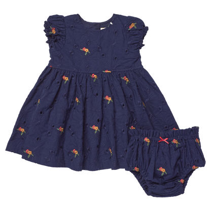 The Pink Chicken Baby Girls' Eliza Eyelet Embroidery Dress Set features navy blue fabric, short ruffled sleeves, delicate navy floral eyelet embroidery, and comes with matching bloomers—the charming set is displayed side by side on a white background.